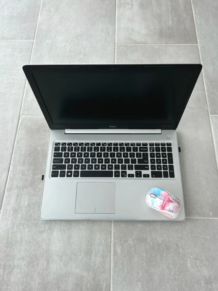 A laptop computer on a tiled floor with a computer mouse beside it, representing an online-only learning setup.